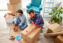 High angle view of a young couple in love sitting on the floor of their apartment, packing things into cardboard boxes, getting ready for relocation Movers and Packers in Dubai.