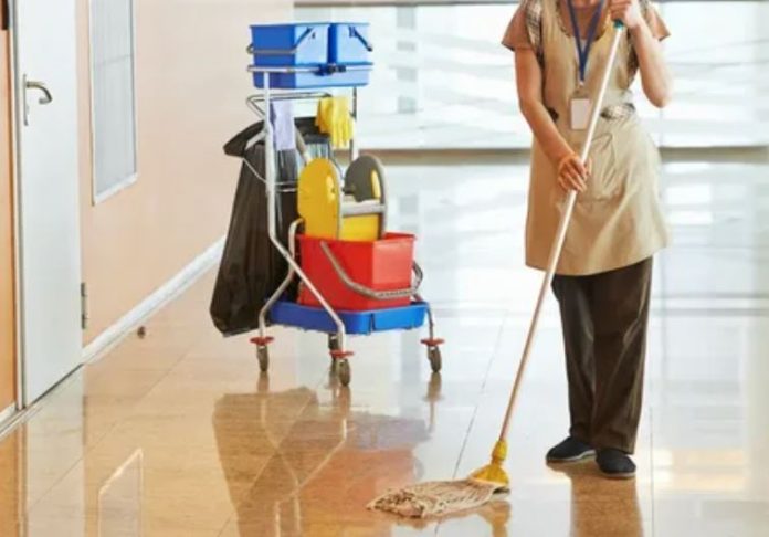 A woman diligently mops a hallway, using a bucket to maintain cleanliness and order in the space.